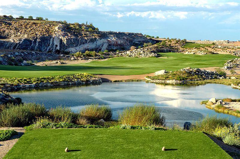 Twilight golf course at Verrado Golf Club in Buckeye, Arizona, featuring a lush green fairway, water hazards, and scenic rocky hills.