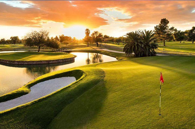 Beautiful golf course at sunset with water hazards, lush green fairways, palm trees, and a red flag on the putting green.
