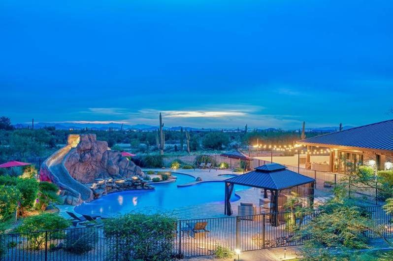 Luxurious Scottsdale estate with a swimming pool, waterslide, outdoor seating, and desert landscape under a twilight sky.