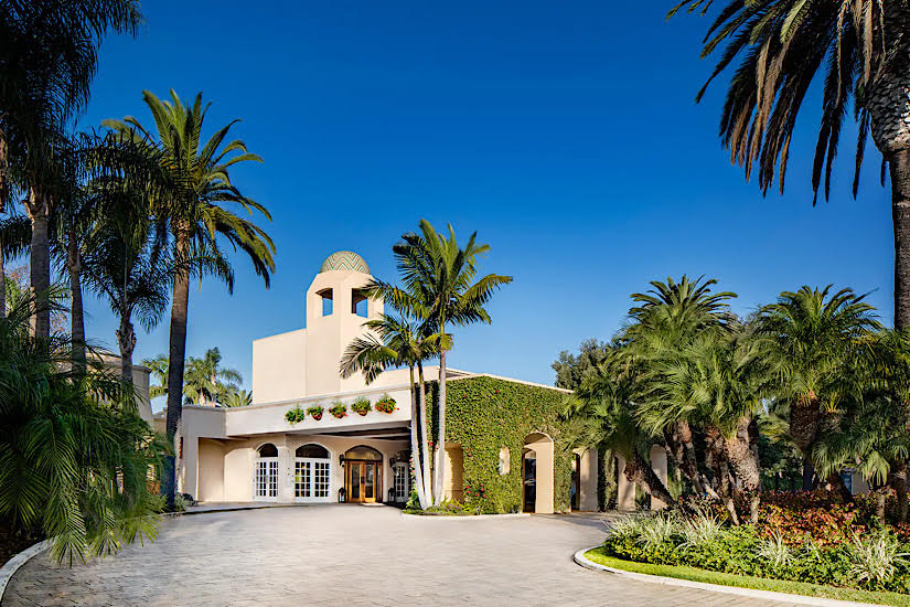Luxurious Hyatt Regency Newport Beach hotel surrounded by palm trees, with a white building and clear blue sky.