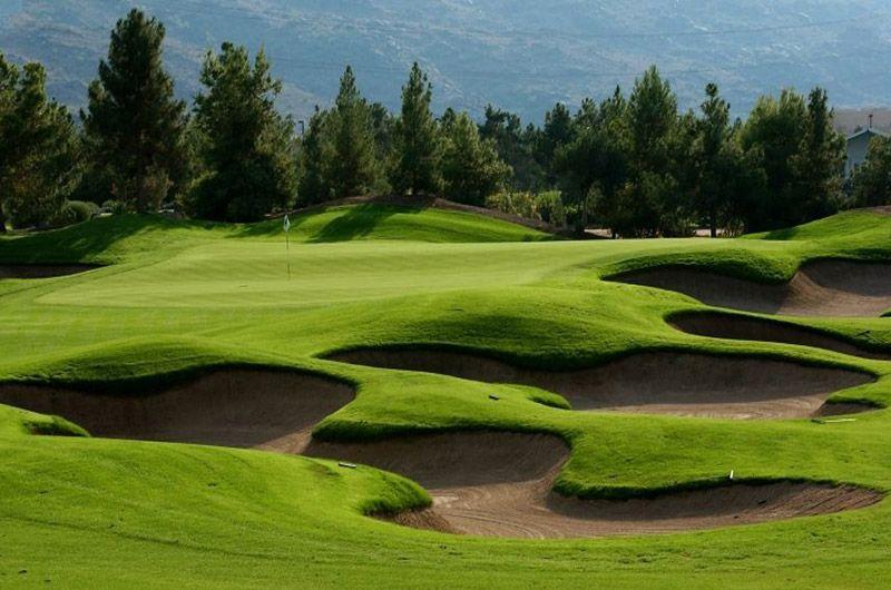 Beautiful golf course in Phoenix/Scottsdale with lush green fairways, sand bunkers, and scenic mountain views at sunrise.