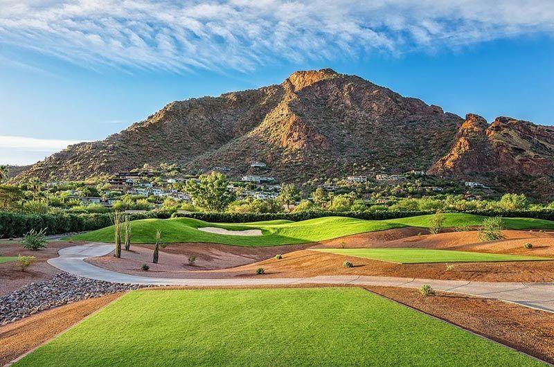 Scenic twilight view of a golf course in Scottsdale with lush green fairways, desert landscaping, and mountains under a blue sky.