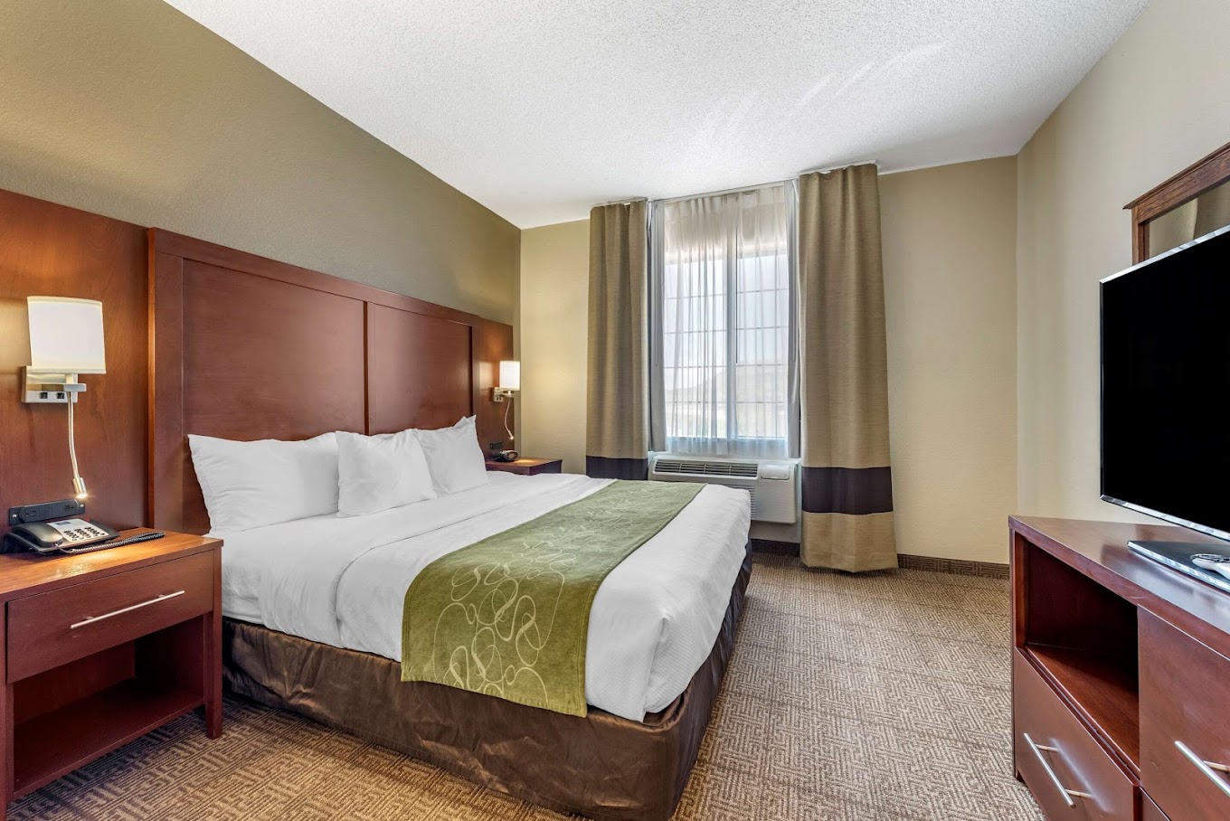 Comfort Suites Castle Rock hotel room with a large bed, wooden furniture, a TV, and a window with curtains, offering a serene ambiance.