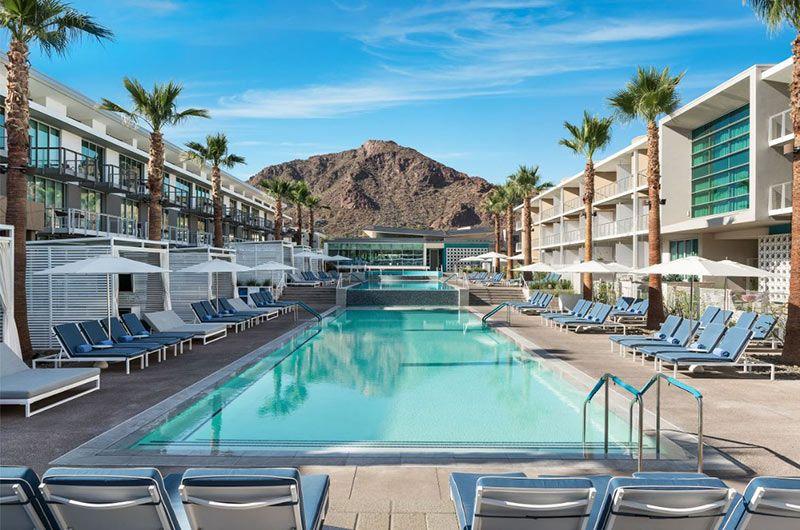 Luxury resort pool area at Mountain Shadows in Scottsdale with palm trees, lounge chairs, and mountain backdrop under blue sky.
