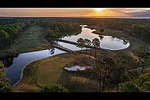 Aerial view of Sea Trail's Willard Byrd Course with tree-lined fairways, water hazards, and a sunset sky in the background.
