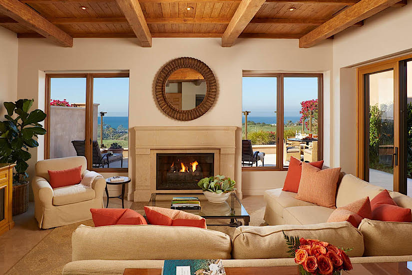 Interior of a luxurious oceanfront villa living room with a fireplace, large windows, and ocean views, decorated with cozy furniture and plants.