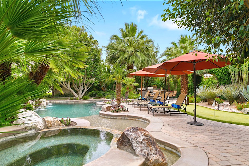 Casa Azul La Quinta, Luxurious backyard with a swimming pool, palm trees, lounge chairs, umbrellas, and lush greenery at Casa Azul La Quinta.