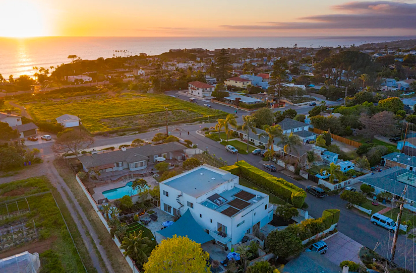 Aerial view of a coastal neighborhood in Cardiff By The Sea, California, during sunset, featuring houses, greenery, and ocean in the background.