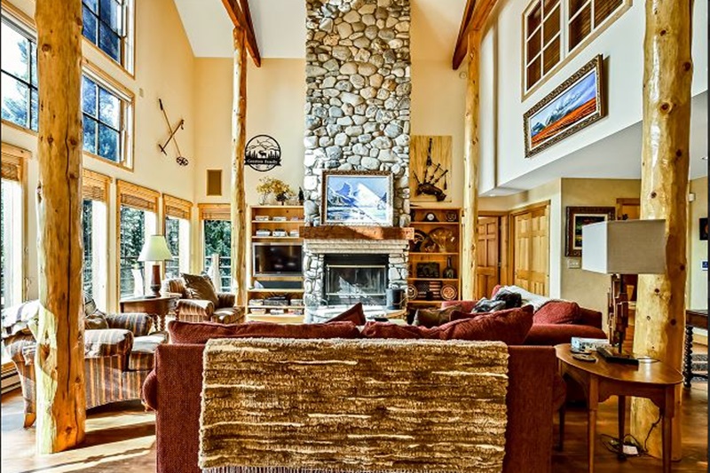 Spacious living room with a stone fireplace, large windows, wooden beams, and cozy seating in a luxury vacation home.