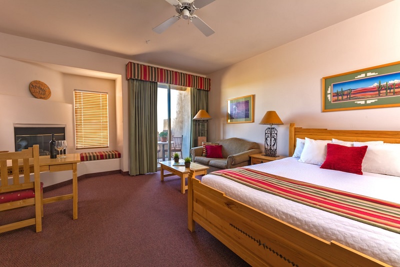 Interior of a cozy hotel room with a large bed, sitting area, balcony, and warm decor, offering a luxurious and relaxing atmosphere.