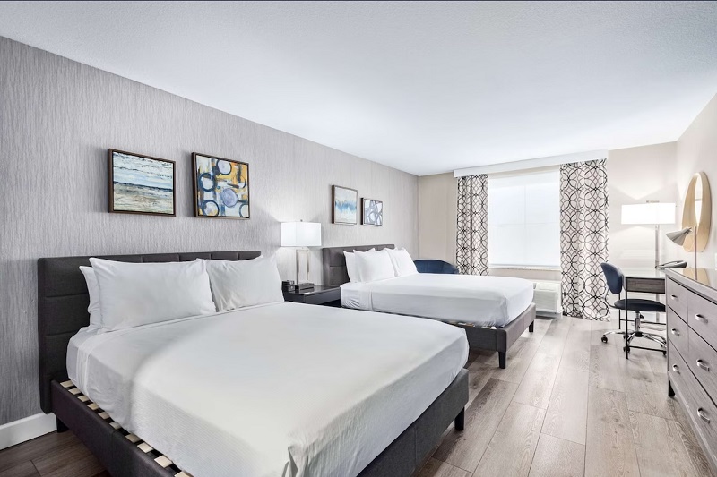 Modern hotel room with two beds, artwork on the wall, a desk, and large window with patterned curtains at Fountain Park Hotel.