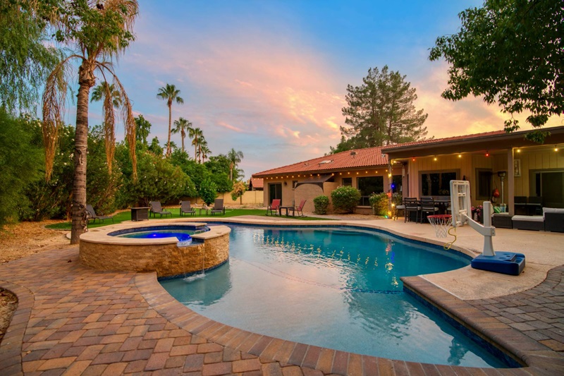 Luxury Scottsdale vacation home with a swimming pool, hot tub, outdoor seating, palm trees, and a sunset sky.