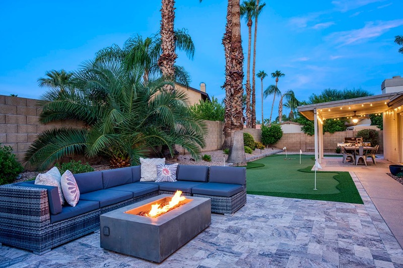 Luxury desert oasis backyard in Scottsdale with a firepit, outdoor seating, palm trees, and a covered dining area at dusk.